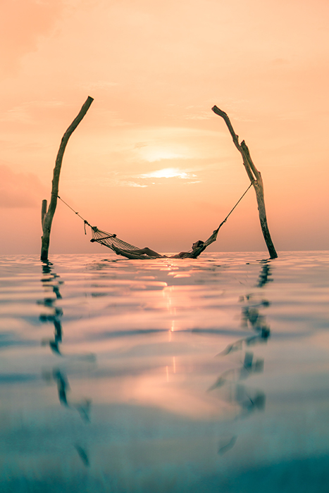 dreamy shot of a person resting on a hammock in the sea at sunset 