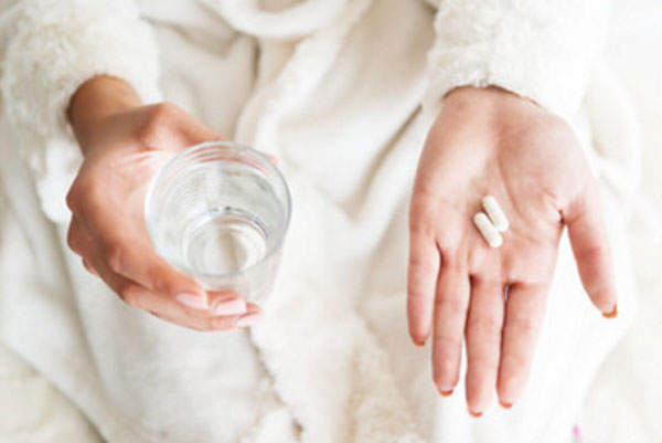 Женщина в одной руке держит стакан с водой, в другой - две капсулы