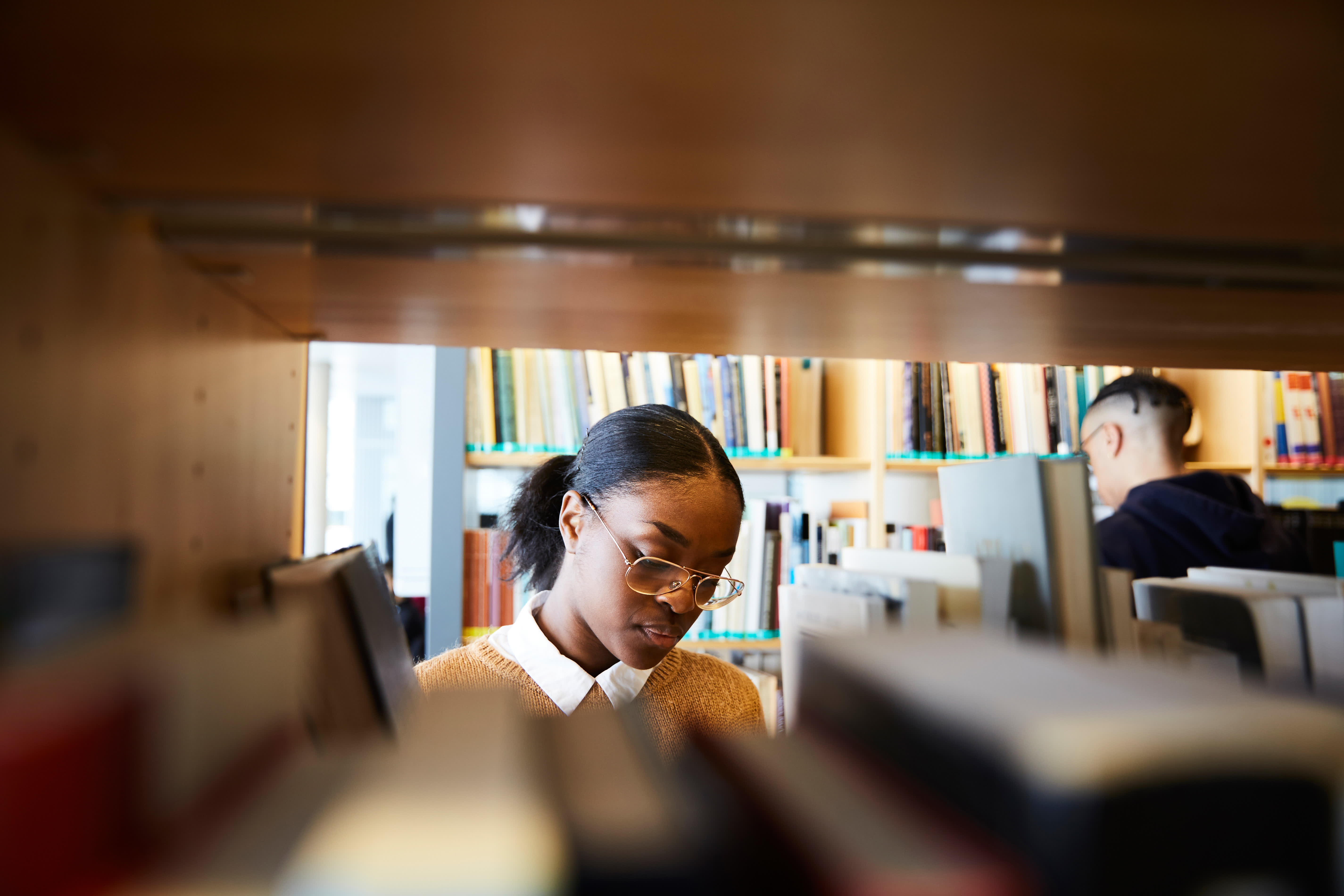 Image of student looking through books on a library shelf.