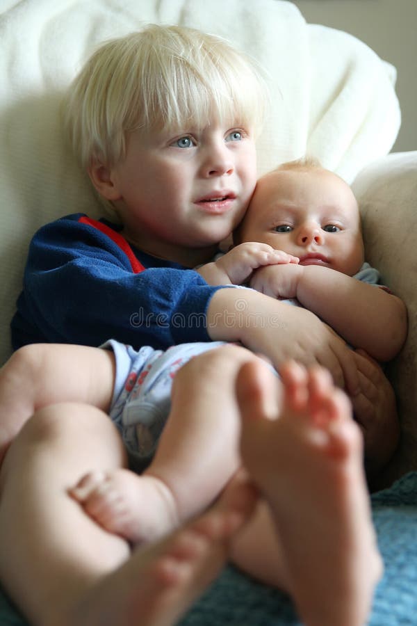Big Brother Snuggling Baby Sister. A toddler aged big brother his hugging his little baby sister as the cuddle on the living room couch watching a movie stock images