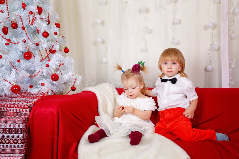 Brother and sister awaiting Christmas. Little brother and sister sitting on the couch near Christmas tree royalty free stock photo