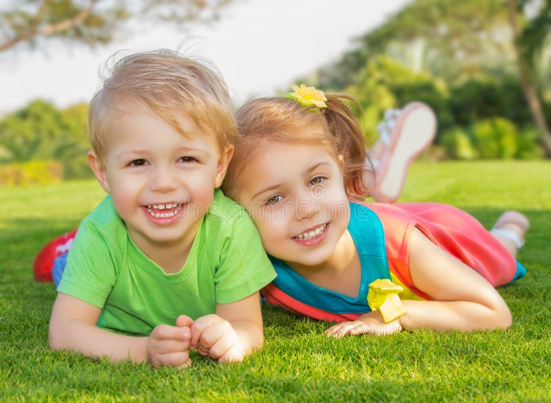 Brother and sister in the park. Picture of brother and sister having fun in the park, two cheerful child laying down on green grass, little girl and boy playing stock photo