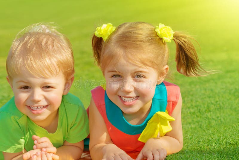 Brother and sister in park. Photo of little brother and sister lying down on green grass field in sunny day, two adorable child playing on backyard, cute friends stock image