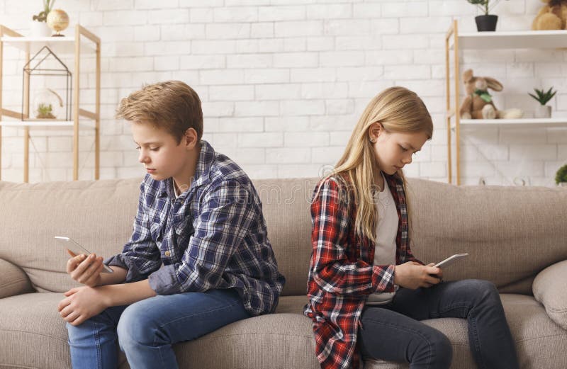Brother And Sister Using Phones Sitting On Couch At Home. Brother And Sister Using Mobile Phones Sitting Back-To-Back Uninterested In Communication On Couch At stock photography