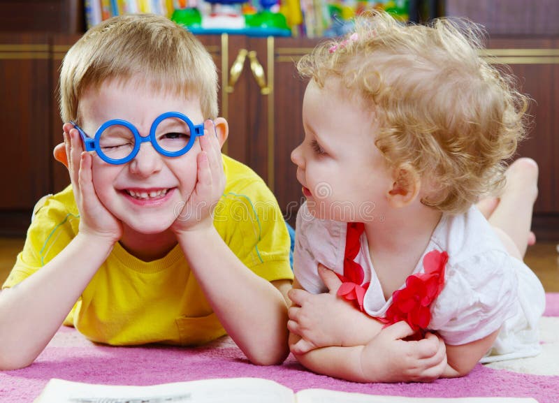 Funny brother in glasses with sister. Funny brother in toy glasses with baby sister on floor stock images