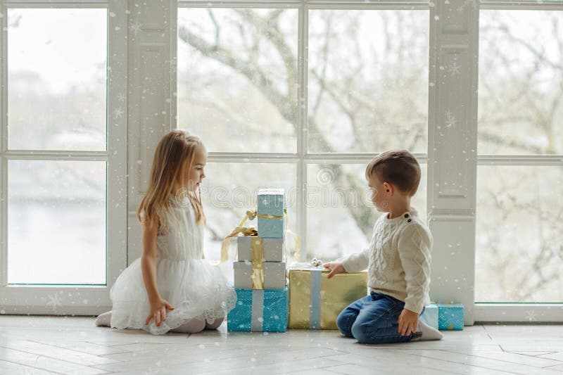 Little adorable brother and sister sitting near a large window i. N the bright New Year`s interior and look at gifts royalty free stock images